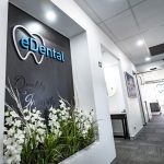 A black wall in eDental Perth (Rivervale) clinic with its logo on it and with decorative flowers at the bottom.