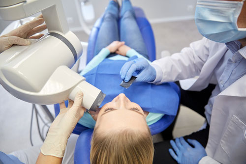 Woman lying on a dental chair along with the dentist and a nurse, which describes the 