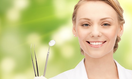 Woman dentist smiling and holding her dentist's tools and that represents the 