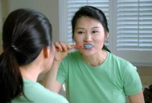 A woman brushing her teeth in front of a mirror represents the 