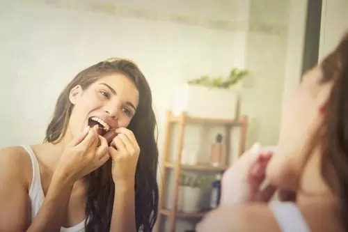 Woman flossing her teeth in front of a mirror, which represents the 